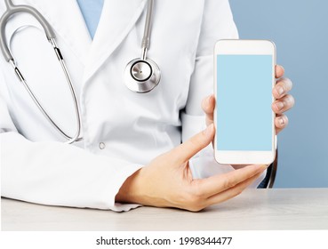 Cropped view of female doctor holding a smartphone with an medical app. Blank blue mockup copy space for text. Online telemedicine support or consultation - Powered by Shutterstock