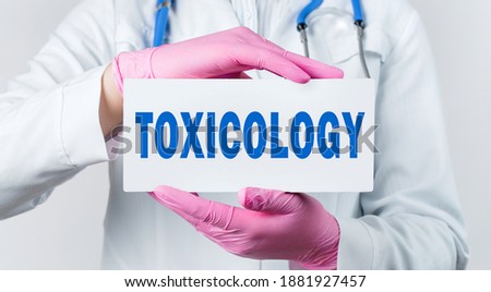 Cropped view of female doctor in a white coat and pink sterile gloves holding a card with word Toxicology. Medical concept
