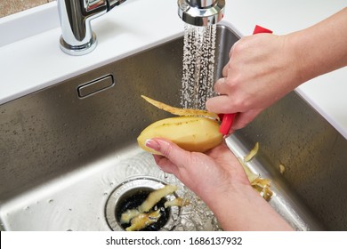 Anbausicht der weiblichen Hände beim Schälen der Kartoffel über Lebensmittelabfallbeseitigungsmaschine