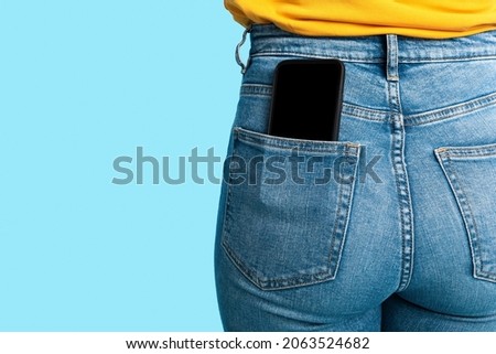 Cropped view of female having cellphone with blank screen in jeans pocket on blue studio background, mockup for mobile app or website. Free space for your advertisement template