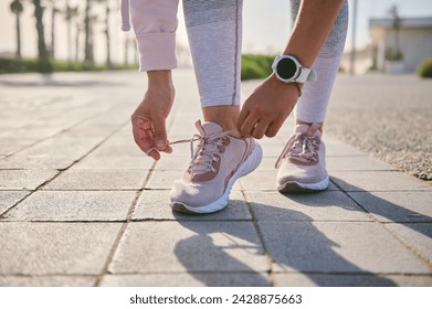 Cropped view of fitness woman in stylish activewear, tying shoelaces of her sporty sneakers before training or running on the treadmill. Getting ready for morning jog outdoor. People and sport concept - Powered by Shutterstock