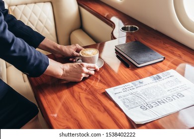 cropped view of flight attendant putting cup of coffee on table in private plane 