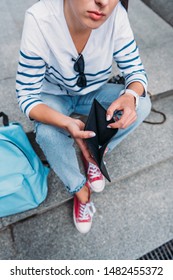 Cropped View Of Girl Holding Empty Black Wallet While Sitting On Stairs 