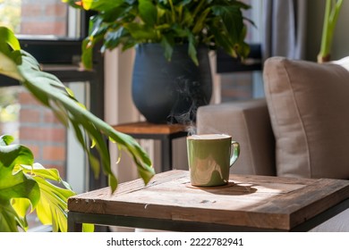 Cropped view of the green mug with tea and steam above it standing at the wooden table - Shutterstock ID 2222782941