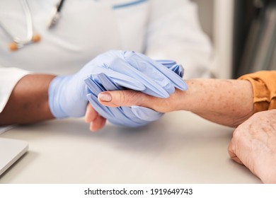 Cropped view of the hand of doctor reassuring her female patient. Multiracial doctor or nurse holding hand of her senior patient while supporting her at the check up. Medical ethics and trust concept