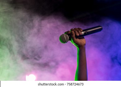 cropped view of hand holding microphone in nightclub with backlit