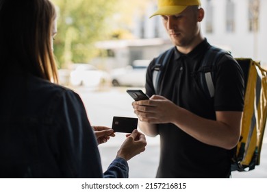Cropped view of hands of caucasian delivery man and young woman at the door, pay by card for online order. Fast home delivery concept.