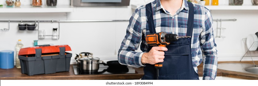 cropped view of handyman holding drill on blurred background in kitchen, banner