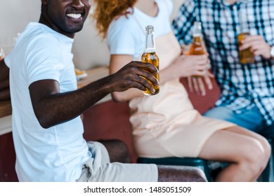 cropped view of happy african american man holding bottle of beer near friends 