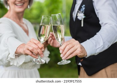 cropped view of happy and mature newlyweds clinking glasses of champagne in green garden - Powered by Shutterstock