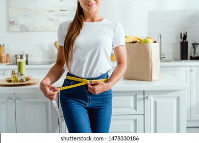 cropped view of happy young woman measuring waist near groceries 
