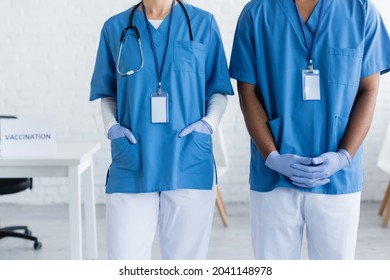 Cropped View Of Interracial Doctors In Uniform With Name Tags In Vaccination Center