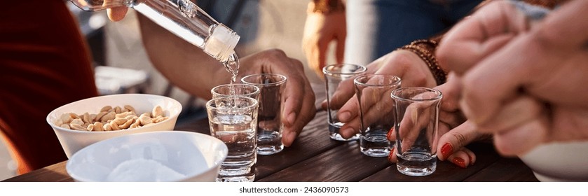 cropped view of interracial young friends pouring tequila shots while at rooftop party, banner - Powered by Shutterstock