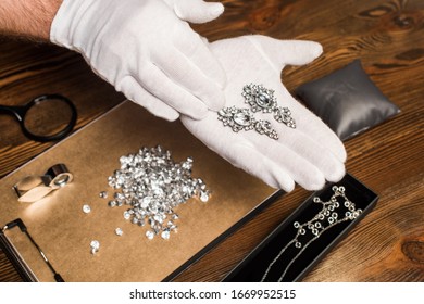 Cropped view of jewelry appraiser holding earrings near gemstones and magnifying glasses on board on table