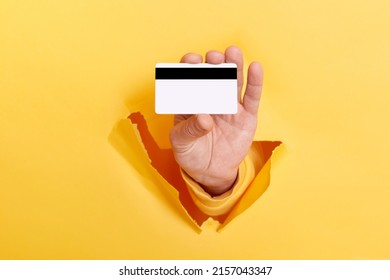 Cropped view of man hand breaks arm through paper and holding credit card, getting bank loan for shopping isolated over yellow background. - Shutterstock ID 2157043347