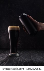 Cropped View Of Man Holding Can Near Glass Of Dark Beer With Foam On Wooden Table