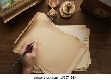 cropped view of man holding fountain pen above vintage paper near painting, candle and old radio on wooden table - Powered by Shutterstock