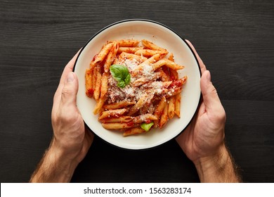 cropped view of man holding plate with tasty bolognese pasta with tomato sauce and Parmesan on black wooden background