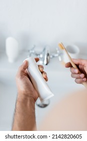 Cropped View Of Man Holding Toothpaste Tube And Toothbrush In Bathroom