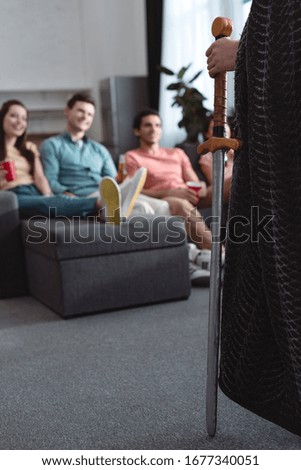 cropped view of man in king costume near smiling friends sitting on sofa
