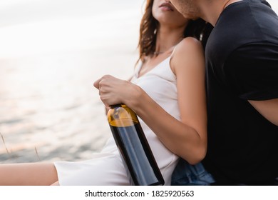 Cropped View Of Man Kissing Girlfriend In Dress With Bottle Of Wine Near Sea