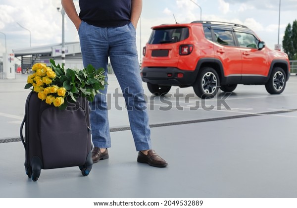 Cropped view of man with luggage and flowers in\
car park outside