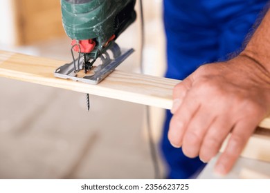 Cropped view of man using a jigsaw machine on wooden plank at home