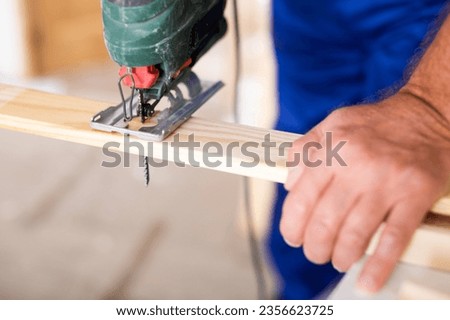 Cropped view of man using a jigsaw machine on wooden plank at home