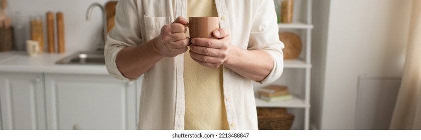 Cropped View Of Man In White Shirt Holding Cup Of Warm Tea In Blurred Kitchen, Banner