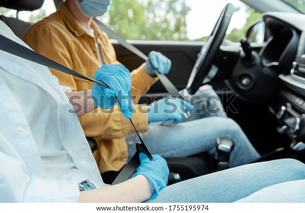 cropped view of man and\
woman in protection gloves fastening seat belts in car during\
covid-19 pandemic