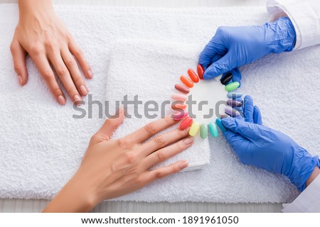 cropped view of manicurist holding palette of multicolored fake nails near client
