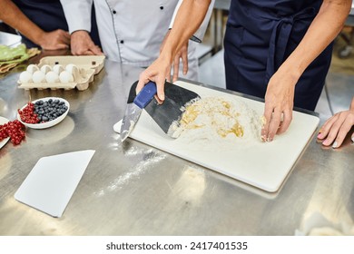 cropped view of mature female chef working with dough next to her colleagues, confectionary - Powered by Shutterstock