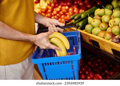 cropped view of mature male customer putting fresh bananas into shopping basket at grocery shop - Powered by Shutterstock