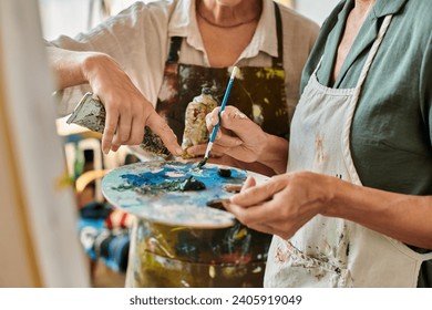 cropped view of mature women in aprons mixing paints on palette during master class in art workshop - Powered by Shutterstock