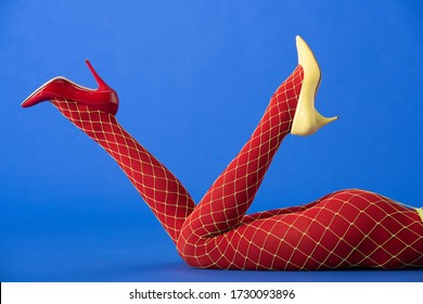 cropped view of model in bright fishnet tights, yellow and red heels lying on blue