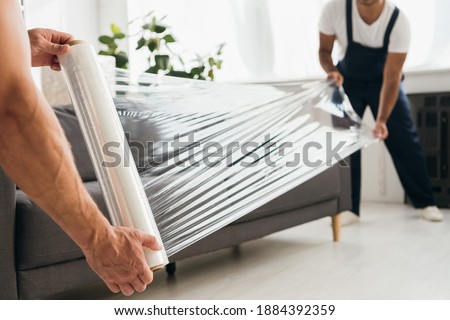 cropped view of movers holding stretch film roll near sofa