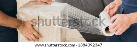 cropped view of movers wrapping box with stretch film, banner