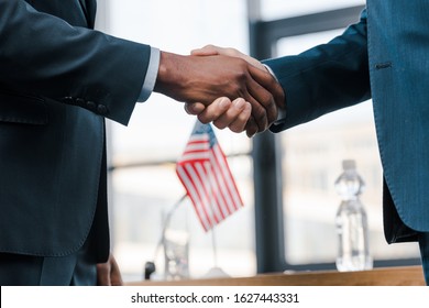 cropped view of multicultural diplomats shaking hands near flag of america