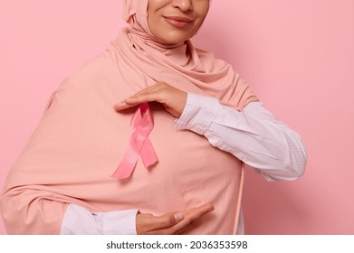 Cropped view of Muslim woman wearing hijab holding pink satin ribbon at chest level to show her support for cancer patients and survivors. World Breast Cancer Awareness Day. Pink background copy space - Shutterstock ID 2036353598