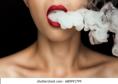 cropped view of naked woman with red lips blowing smoke, isolated on black  