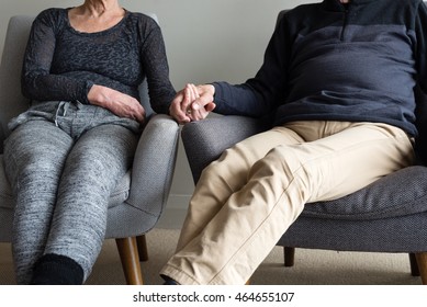 Cropped View Of Older Couple Dressed In Contemporary Clothing, Seated In Armchairs And Holding Hands