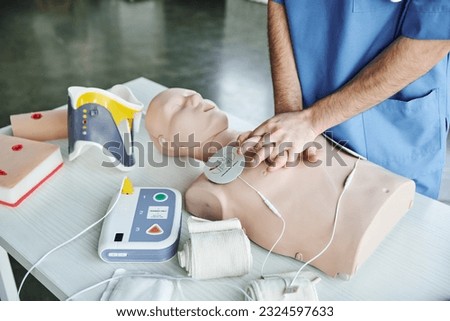 cropped view of paramedic doing chest compressions on CPR manikin near defibrillator, compressive bandages and wound care simulators, emergency situations response concept