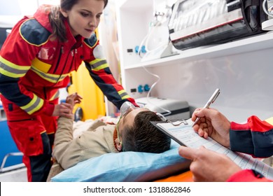 Cropped view of paramedic writing diagnosis while colleague checking pulse