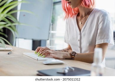 cropped view of pierced businesswoman with pink hair typing on computer keyboard