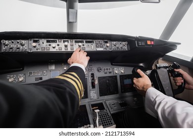 Cropped View Of Pilot Reaching Control Panel Near Co-pilot Using Yoke In Airplane Simulator