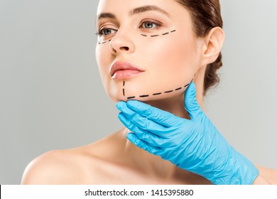 cropped view of plastic surgeon touching face of attractive woman with marked face isolated on grey 