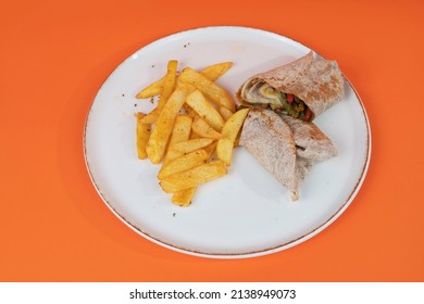 Cropped view of plate of meat wrap and french fries with green and red peppers shot from side or angle with selective focus on isolated setting, orange background.