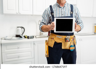 Cropped View Of Plumber In Tool Belt Holding Digital Tablet In Kitchen