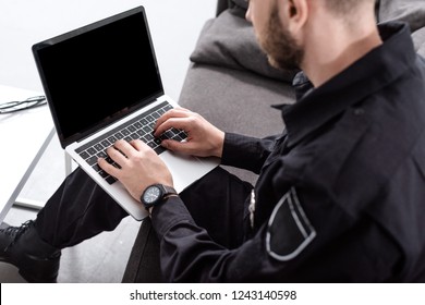 cropped view of police officer sitting on couch and typing on laptop keyboard