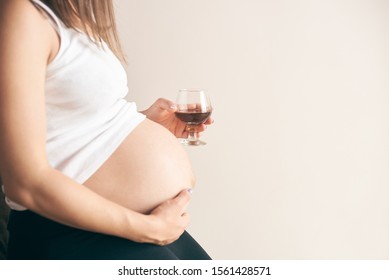 Cropped view of pregnant woman with big belly sitting at home and drinking red wine. Future mother leading unhealthy lifestyle during pregnancy period. Concept of threat and harmfulness.